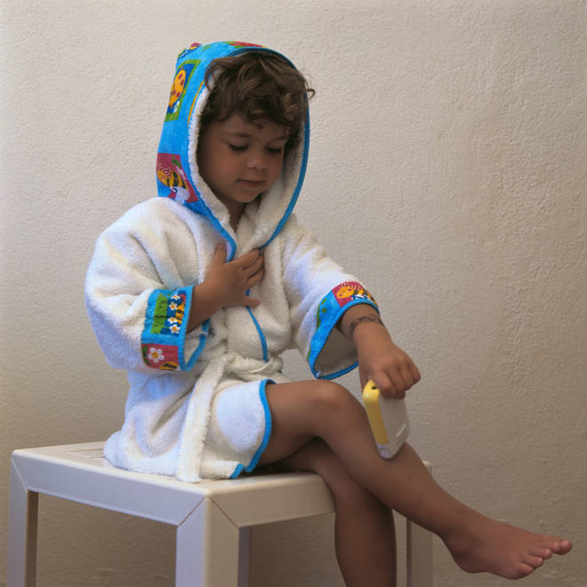 Girl wearing bathrobe, sitting on table, pretending to shave legs