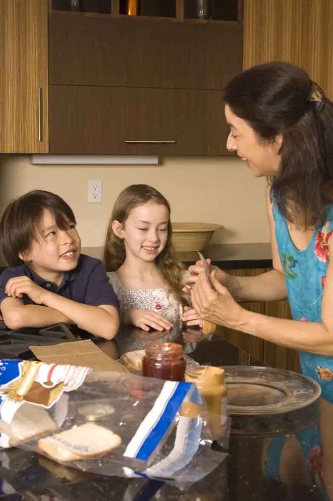 Stock image of a woman making her children peanut butter sandwiches