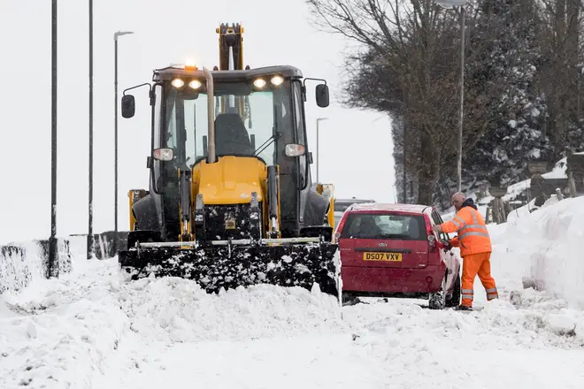 A car receives help from a gritter as it gets stuck in snow