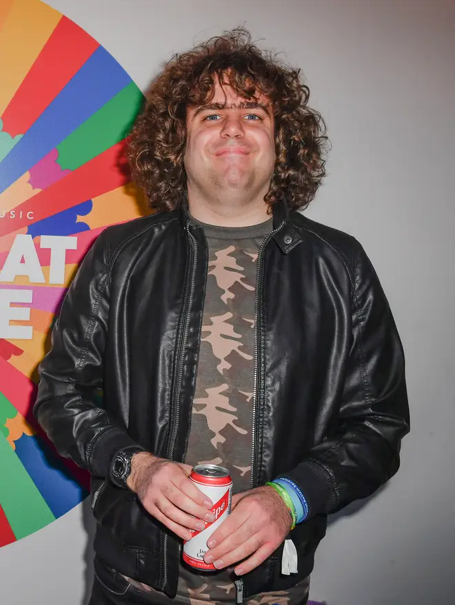Daniel Wakeford smiles in a camouflage t-shirt and leather jacket