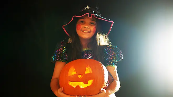 Girl wearing a witch outfit holding a pumpkin