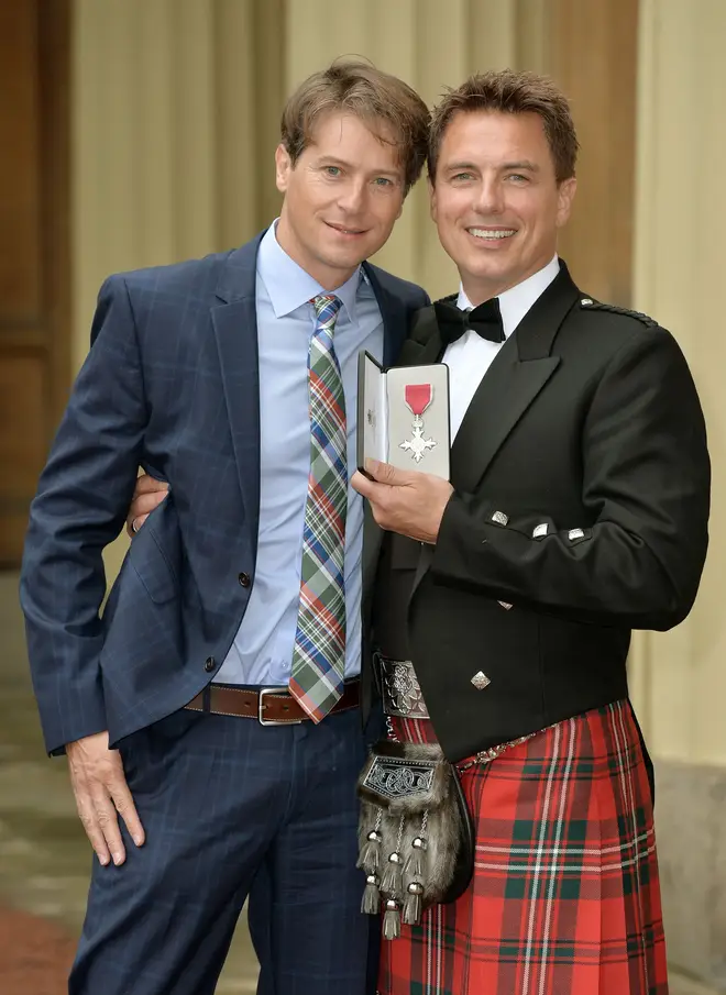 John poses with husband Scott Gill after being awarded an MBE