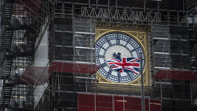 The clock face peeks out from scaffolding.