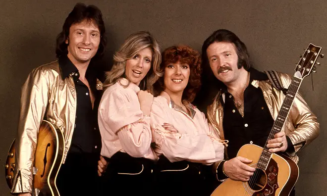 Brotherhood of Man posing with guitars with the girls wearing pink jackets and the men wearing gold jackets
