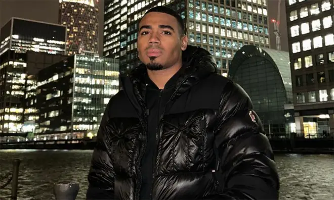 Tyrique Hyde in a black coat standing in the city at night time