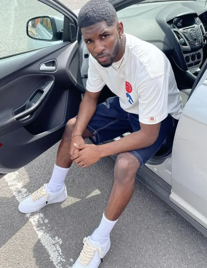 André sitting in his car posing while wearing a white t-shirt and denim shorts