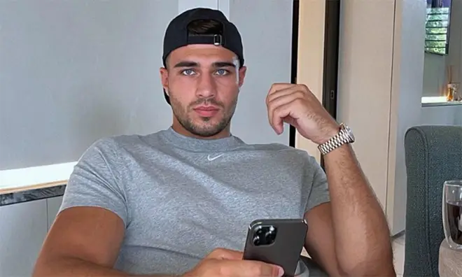 Tommy Fury wearing his cap backwards wearing a grey t shirt and holding his phone