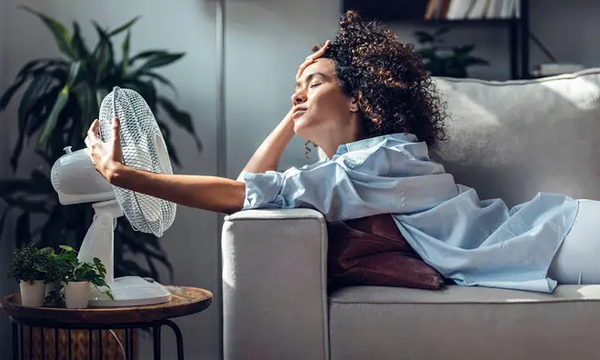 Woman laying on a sofa holding a white fan on her face