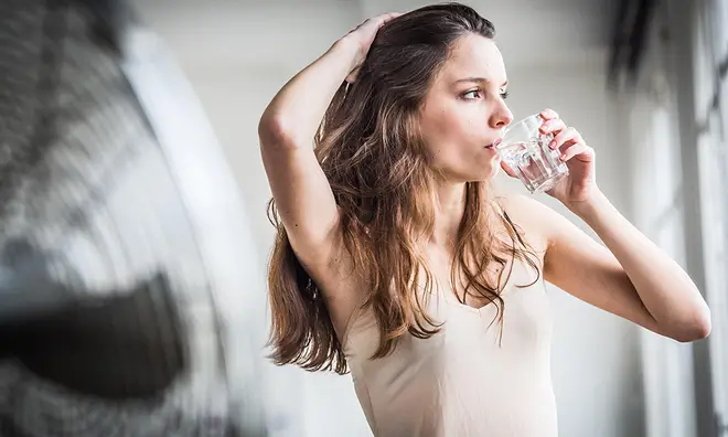 Woman standing in front of a fan drinking a class of water