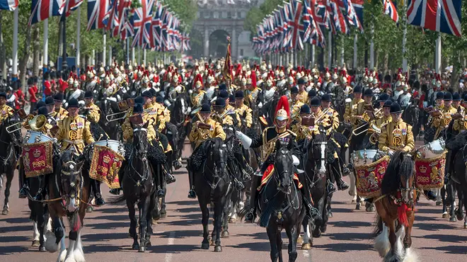 Trooping the Colour procession back to Buckingham Palace featuring The Mall lined with Union Jack flags and hundreds of soldiers and military members