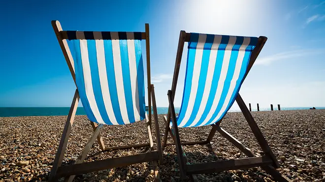 Two blue and white deck chairs on a pebble beach in the sunshine