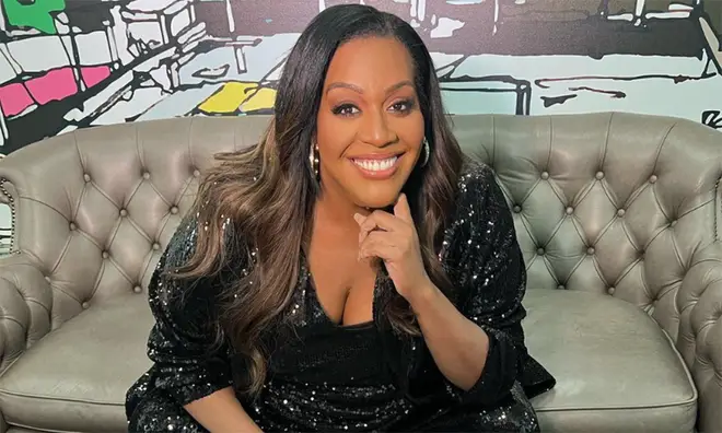Alison Hammond wearing black sequins sitting on a grey sofa smiling