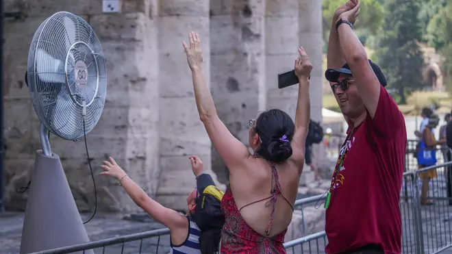 Sweltering tourists pictured at the colosseum in Rome cooling down in front on a fan