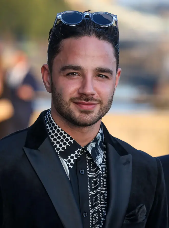 Adam Thomas wearing a black suit and printed shirt as he stands on the red carpet