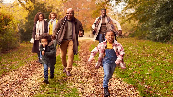 A family having lots of fun and running in a park in autumn as leaves are on the floor