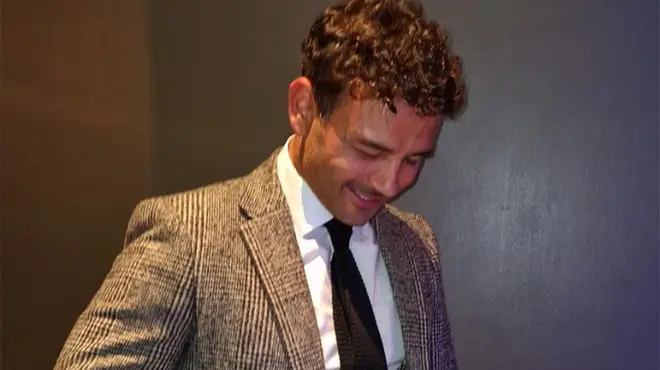 Ryan Thomas looking down and smiling while wearing a suit