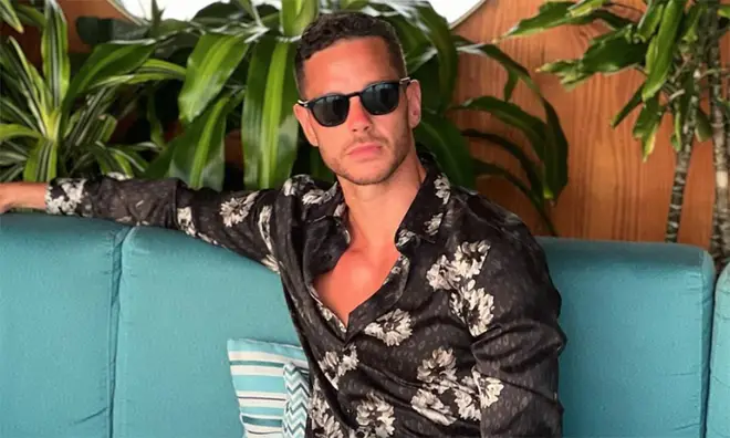 Scott Thomas wearing a floral black shirt and sunglasses while sitting on a turquoise green sofa