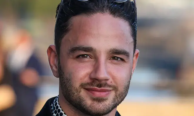 Adam Thomas smiling on the red carpet in a black blazer and monochrome shirt