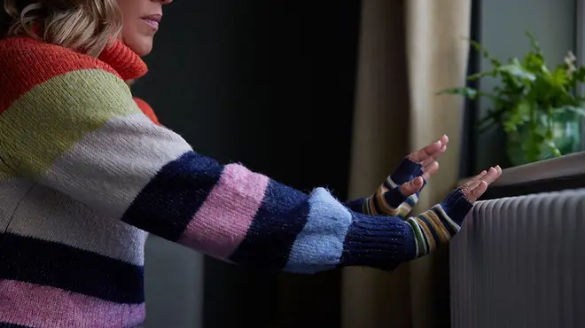 Woman wearing colourful stripey jumper warming her hands up on radiator