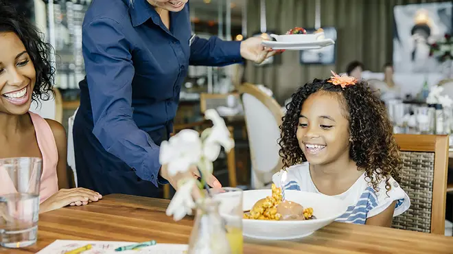Young girl smiling as waitress delivers her food