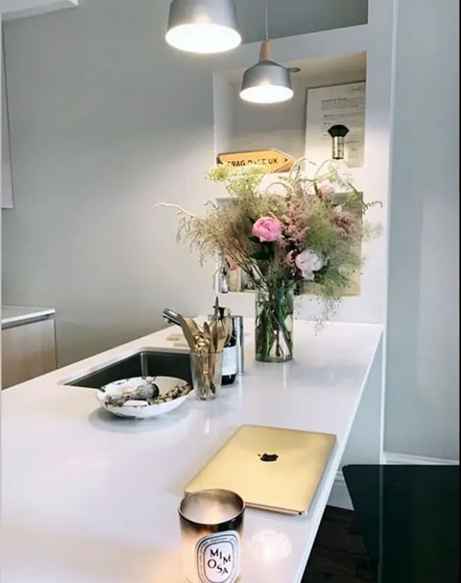 The stunning white kitchen has a bunch of fresh flowers and a Diptyque candle