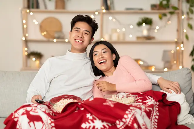 Couple watching Christmas movies under a red blanket