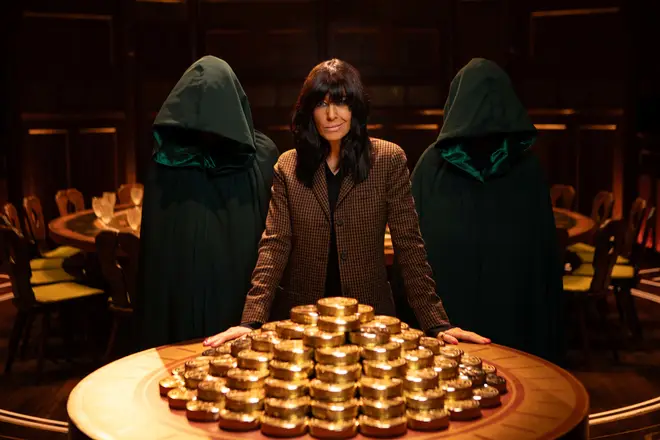 Claudia Winkleman poses with cloaked figures and gold coins