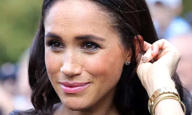Meghan Markle tucking her hair behind her ear and smiling