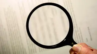 Reading the fine print of a contract/ agreement using a magnifying glass. ASX Au
